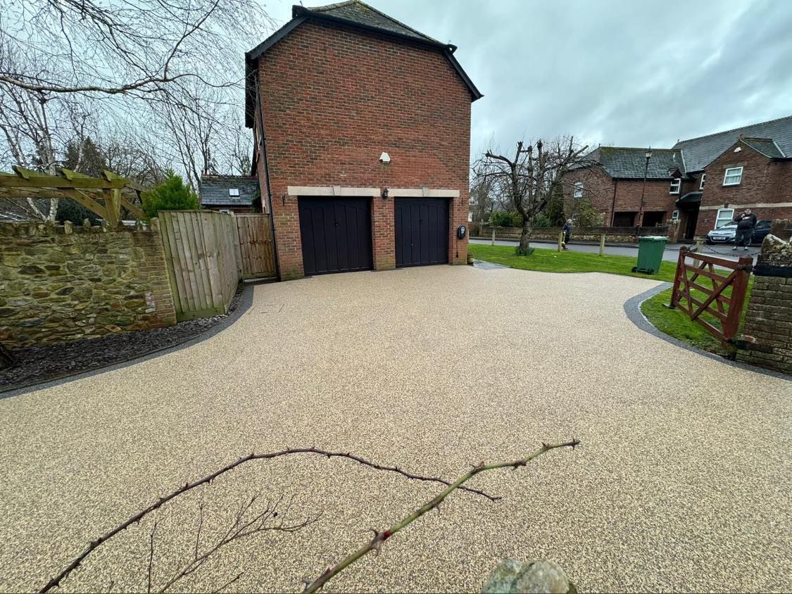 A gravel driveway leading to a two-story brick building with two black garage doors under a cloudy sky.