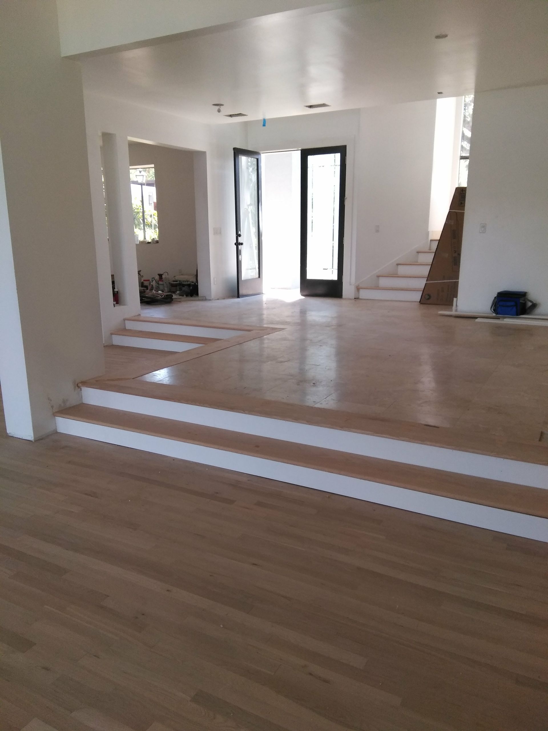 A large empty room with wooden floors and white stairs