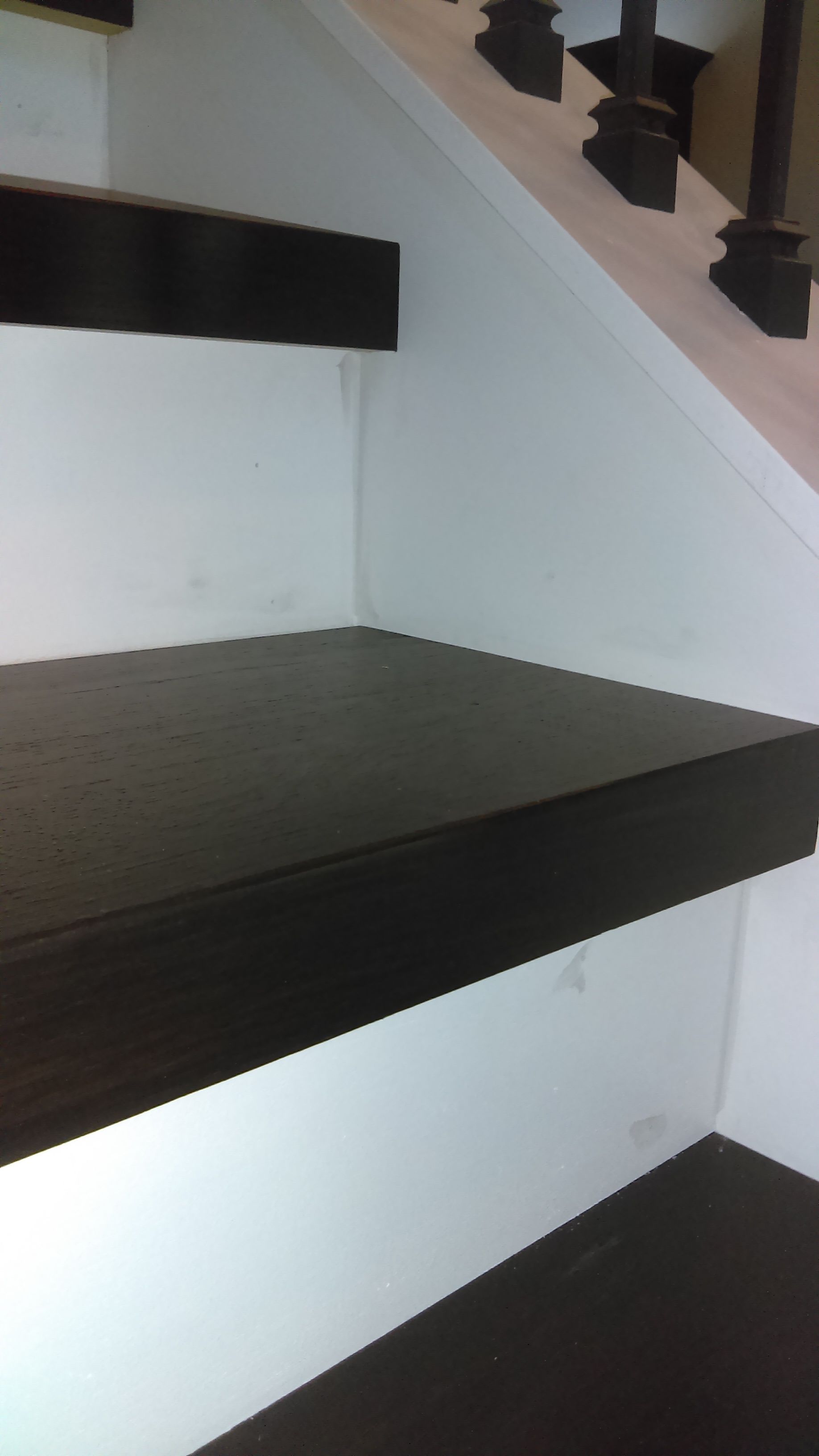 A close up of a wooden staircase with a white wall