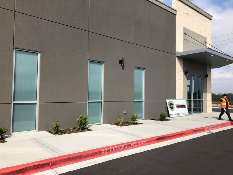 A man in an orange vest is walking down a sidewalk in front of a building.