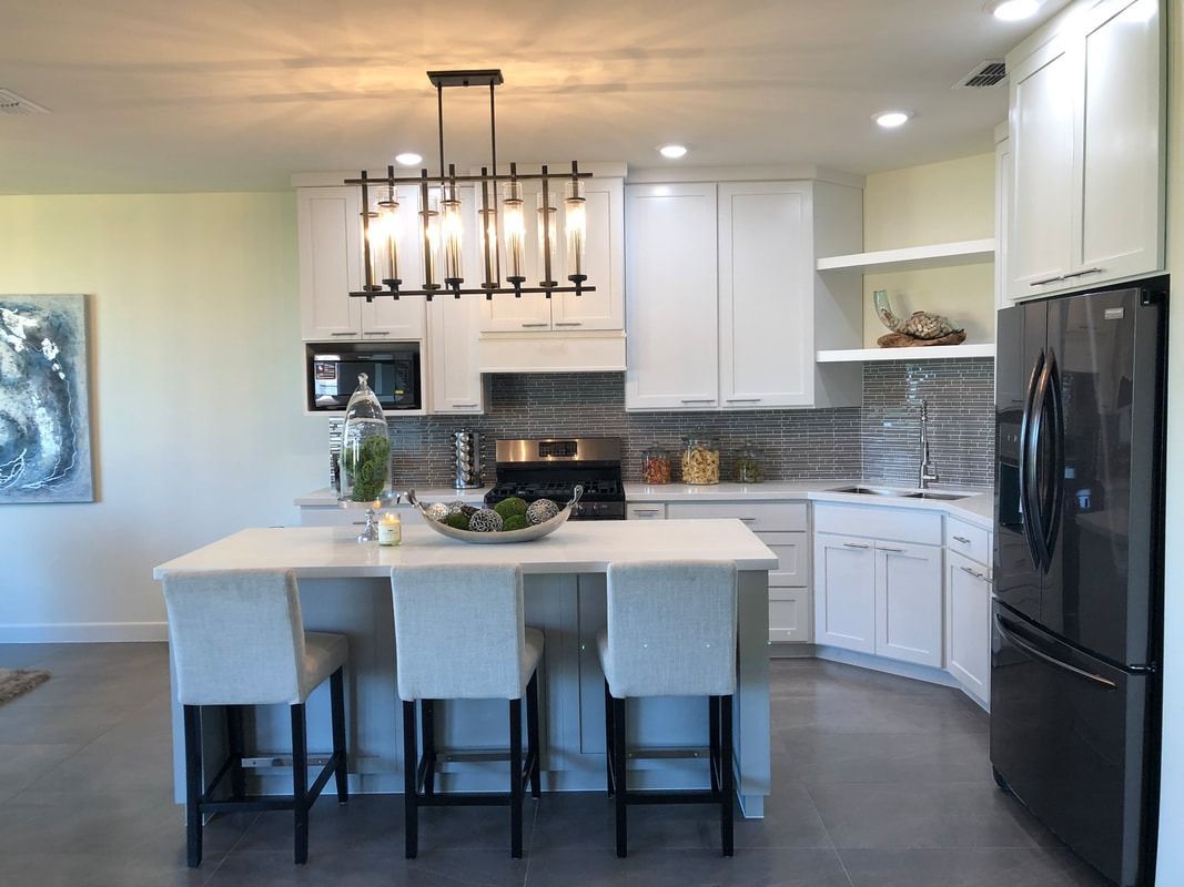 A kitchen with white cabinets , a large island , and a black refrigerator.