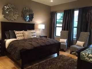 A bedroom with a large bed , two chairs , a rug and two mirrors on the wall.
