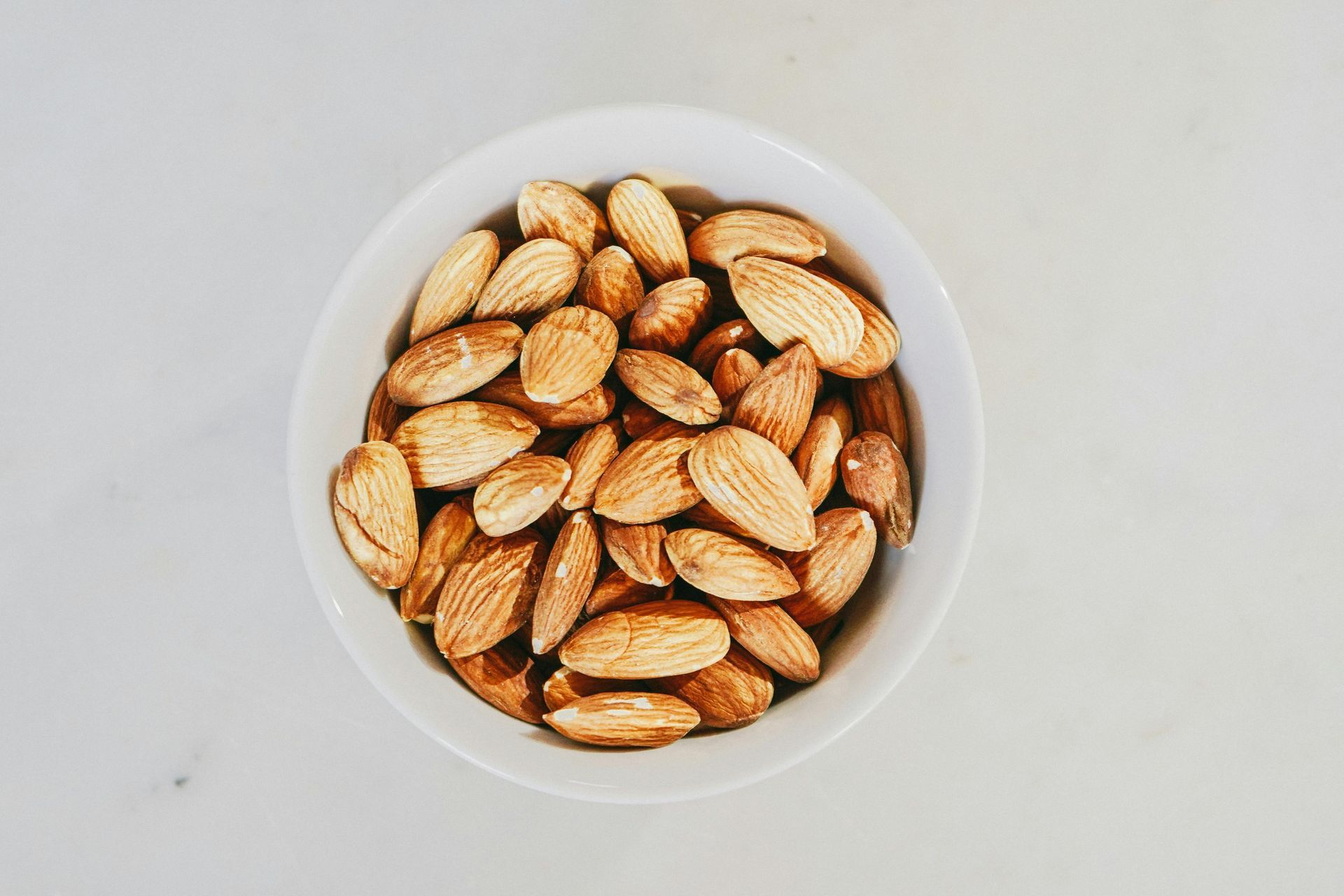 Bowl of roasted almonds on a white surface.