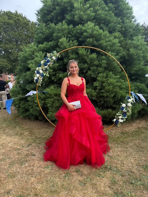 Woman in a red formal dress, posing outdoors near a gold circle decoration with flowers.