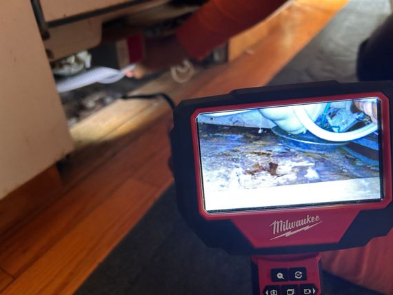 A person is using a milwaukee inspection camera to look under a cabinet.