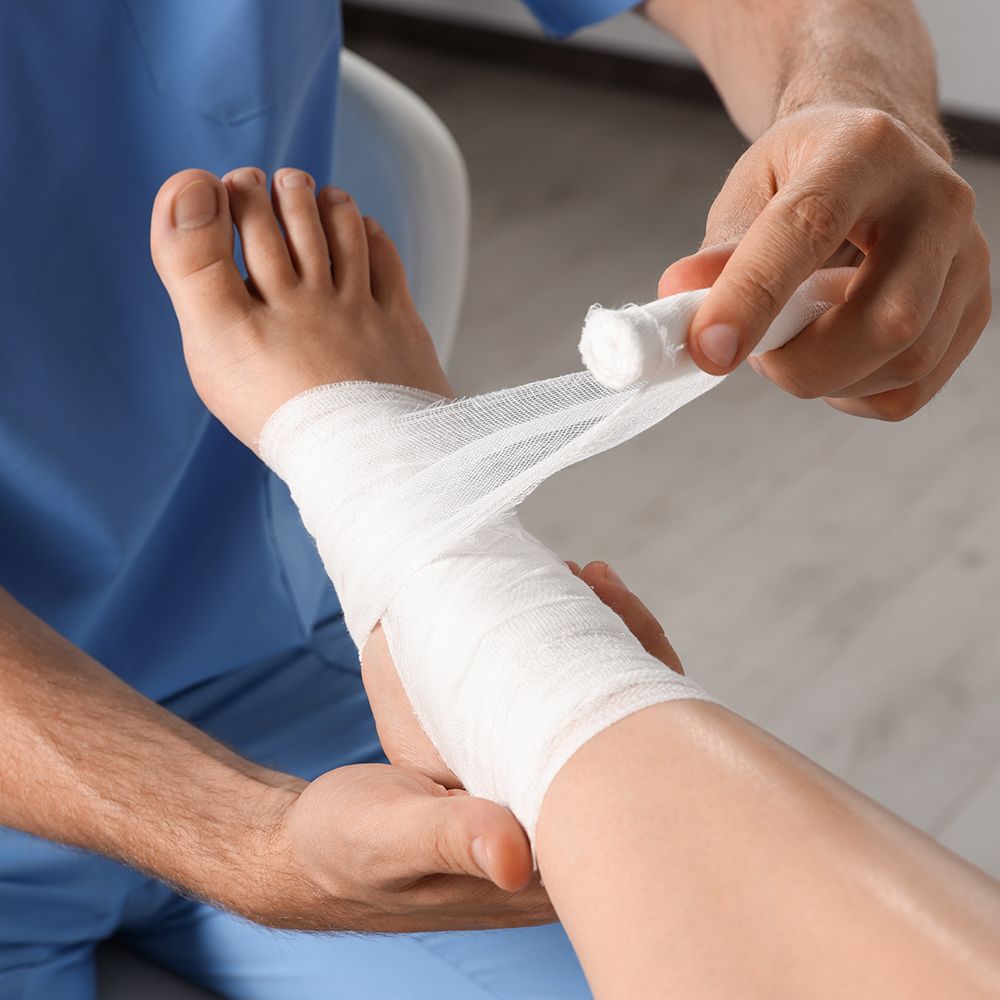 Person wrapping a bandage around another person’s injured ankle in a medical setting.