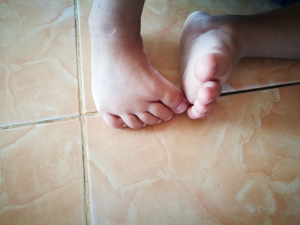 Bare feet on tiled floor, one foot flat, the other flexed.