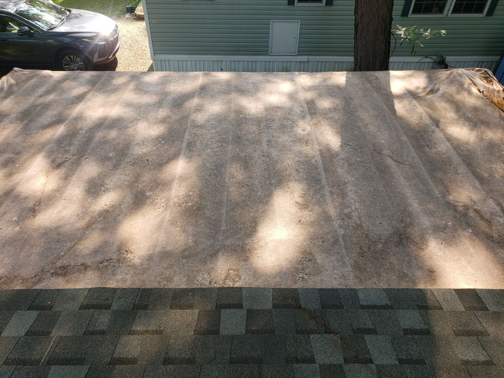 View of roof covered in sand-like material, possibly for repair, with a car and building in the background.