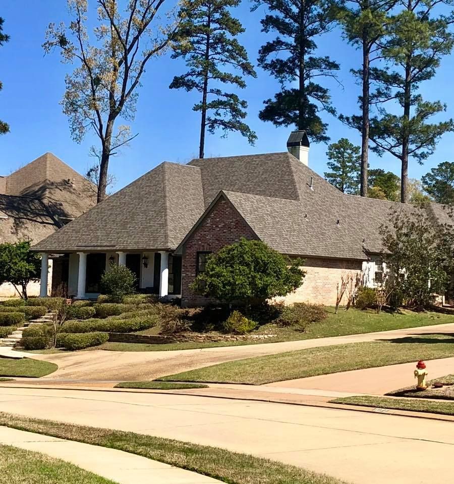 A brick house with a gray roof is surrounded by trees