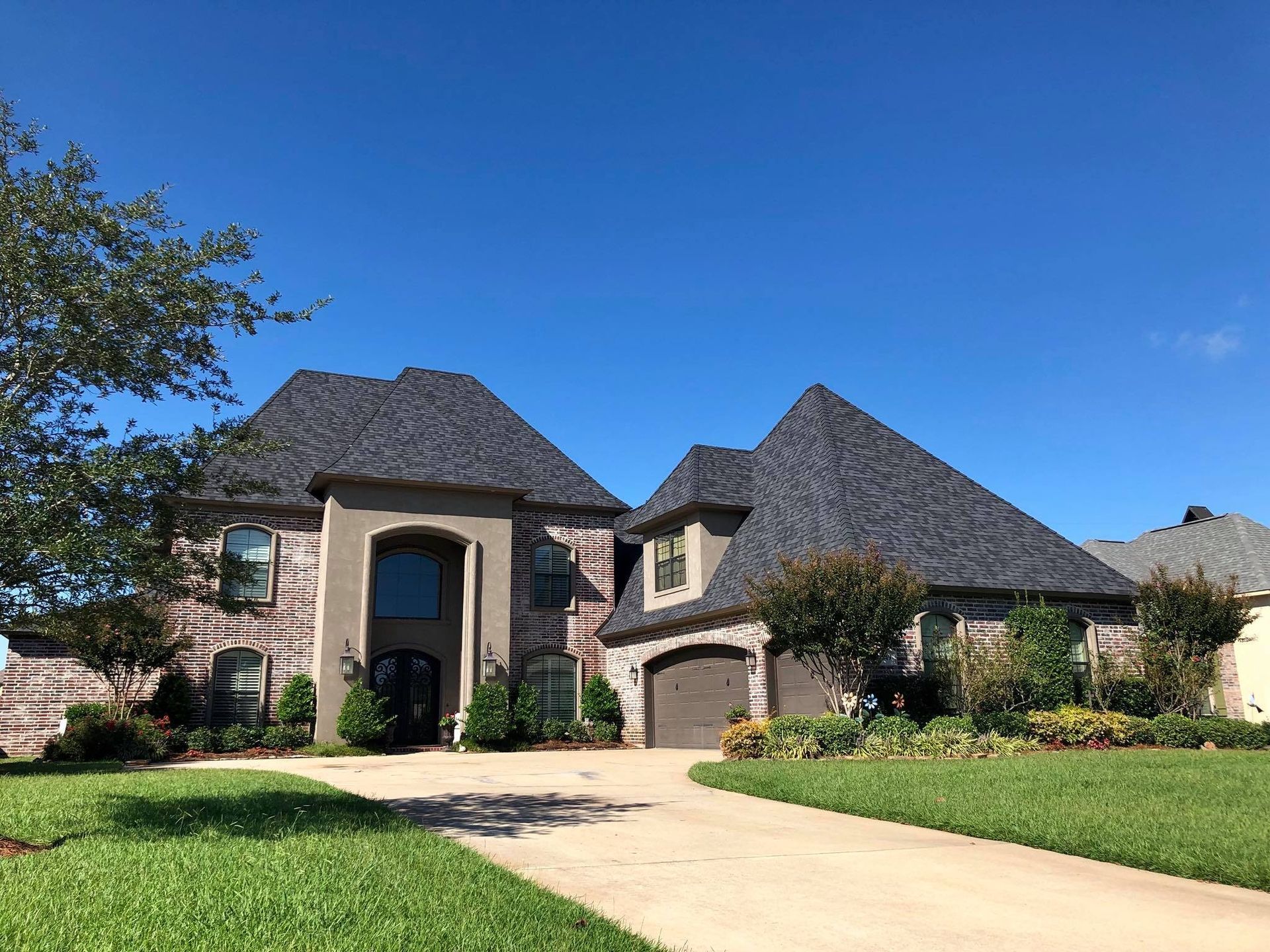 A large brick house with a gray roof is sitting on top of a lush green lawn.