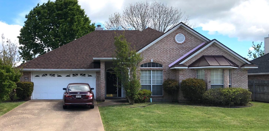 A red car is parked in front of a brick house