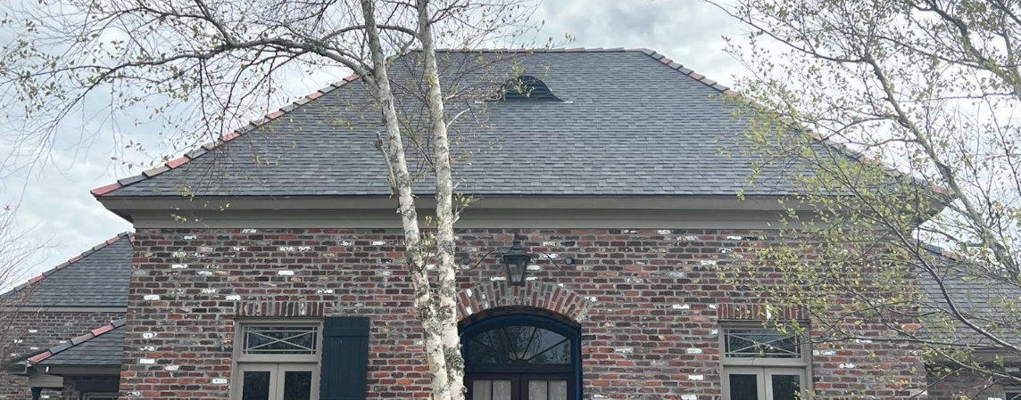 A large brick house with a black roof and trees in front of it.