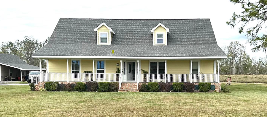 A yellow house with a gray roof and a porch.