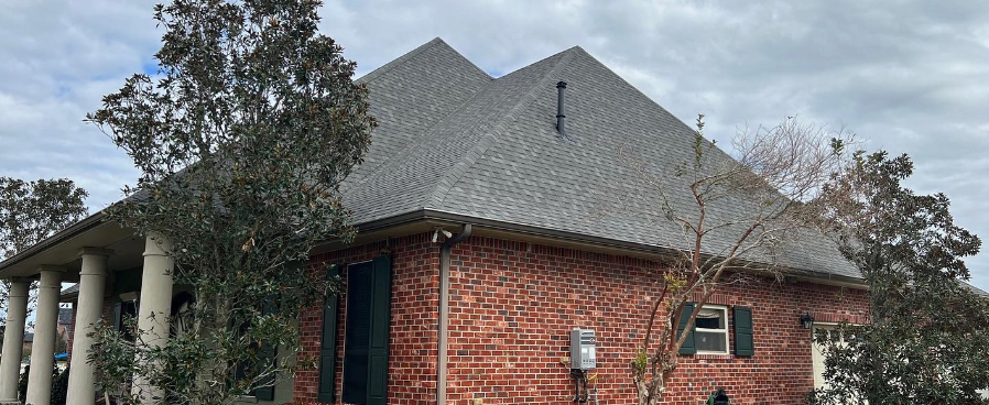 A large brick house with a gray roof and trees in front of it.