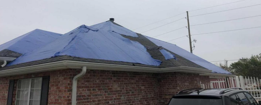 A blue tarp is covering the roof of a brick house.