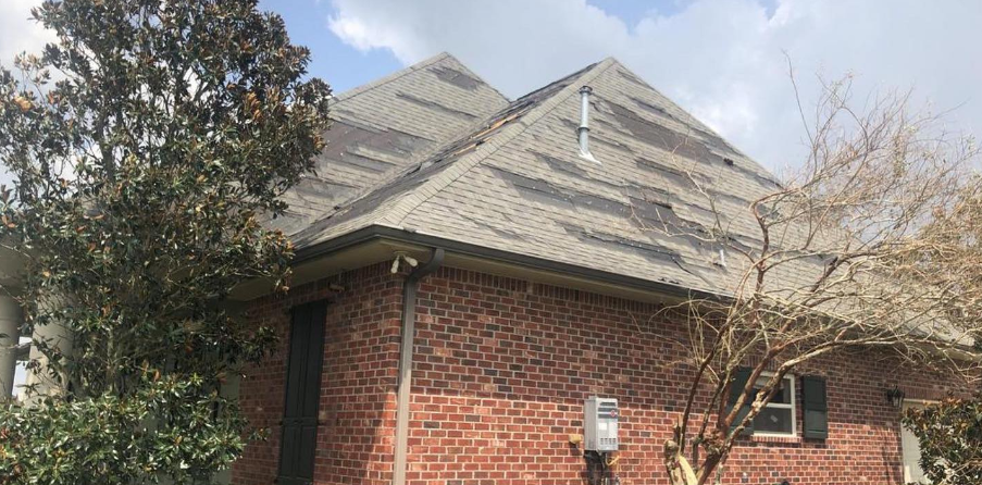 A brick house with a gray roof and a tree in front of it.