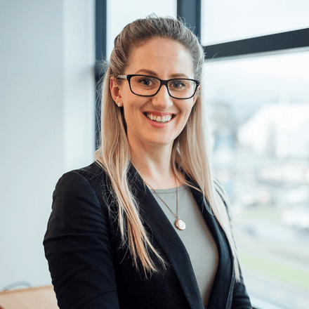 A woman wearing glasses and a black jacket is smiling for the camera.