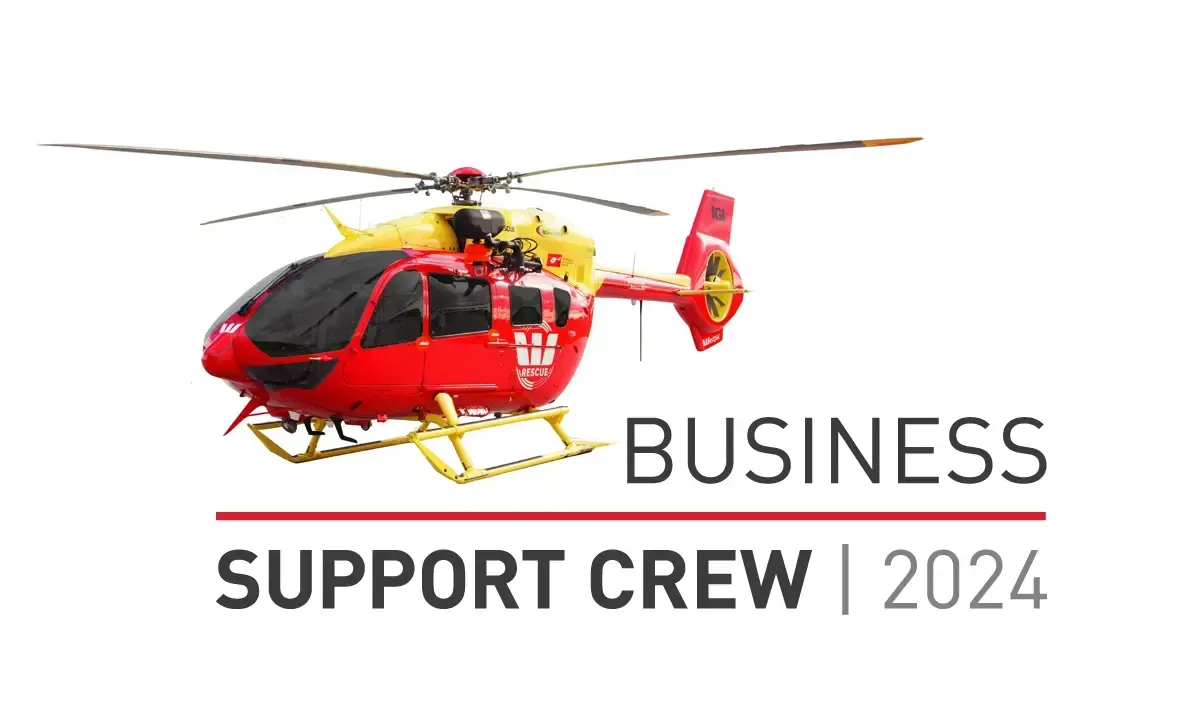 A red helicopter is flying over a sign that says `` business support crew 2024 ''.