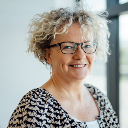 A woman with curly hair and glasses is smiling for the camera.