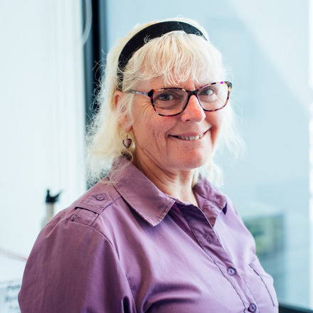 A woman wearing glasses and a headband is smiling for the camera