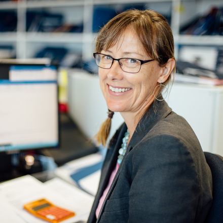 A woman wearing glasses is smiling while sitting in front of a computer