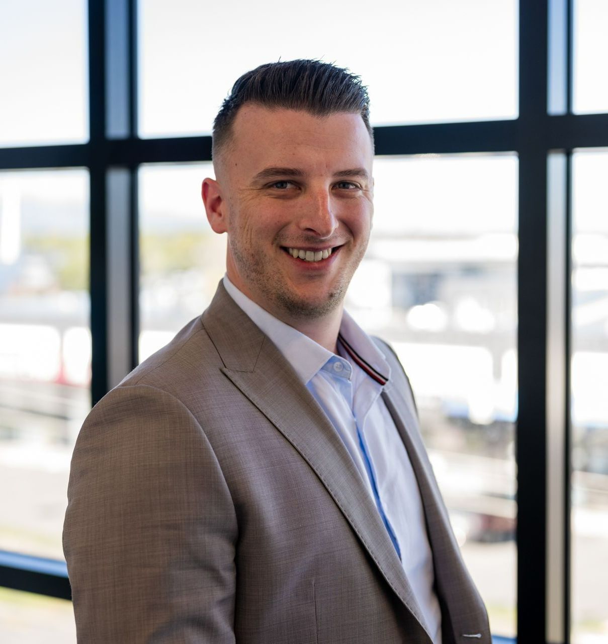 A man in a suit is smiling in front of a window.
