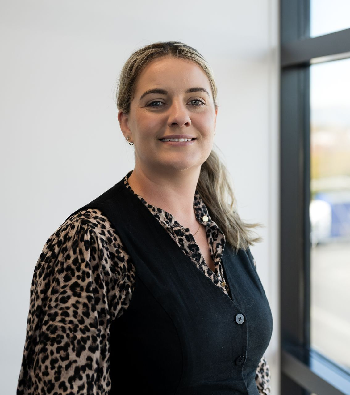 A woman wearing a leopard print shirt and a black vest smiles for the camera