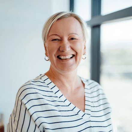 A woman in a striped shirt is smiling in front of a window.