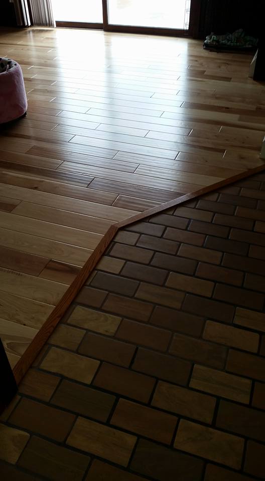 A dog bowl is sitting on a wooden floor next to a brick floor.