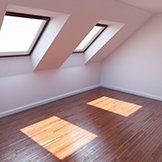 An empty room with a wooden floor and two skylights on the ceiling.