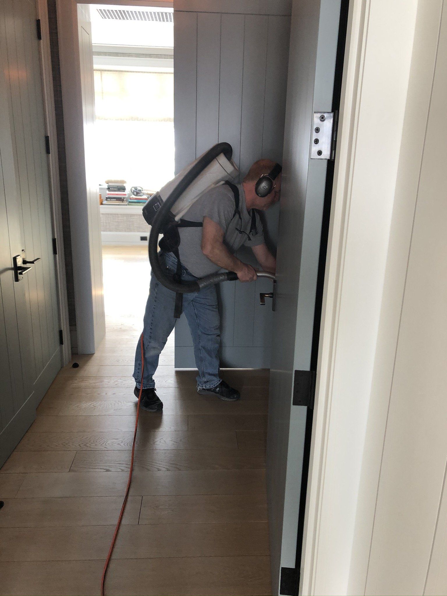 A man wearing headphones is using a vacuum cleaner to clean a door