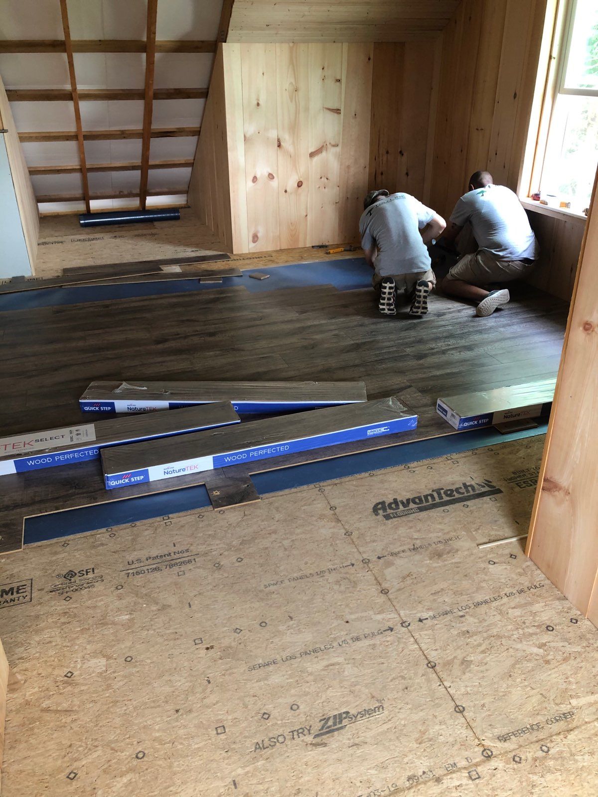 Two men are working on a wooden floor in a room.