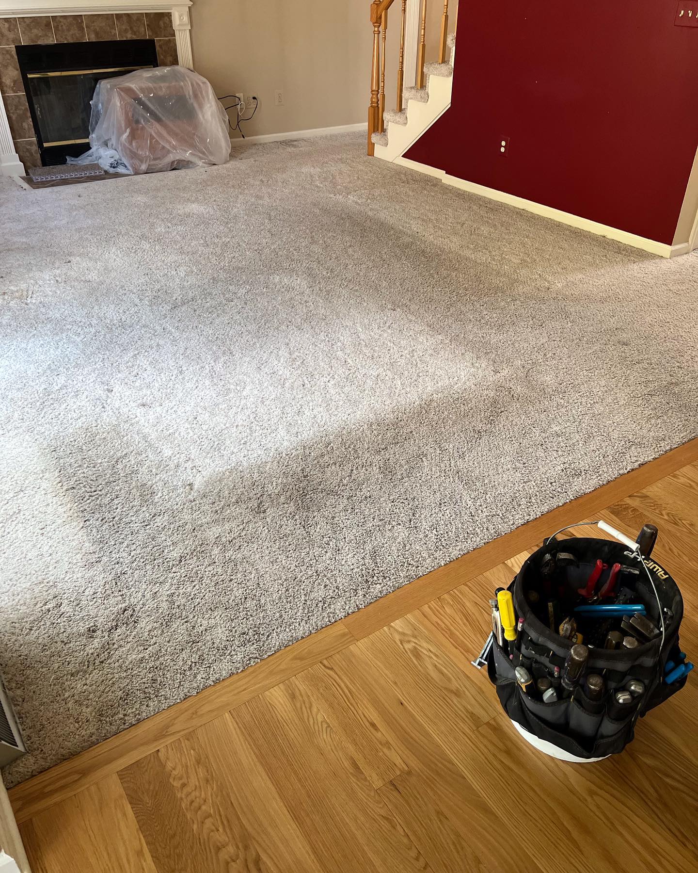 A bucket of tools is sitting on the floor in a living room next to a fireplace.