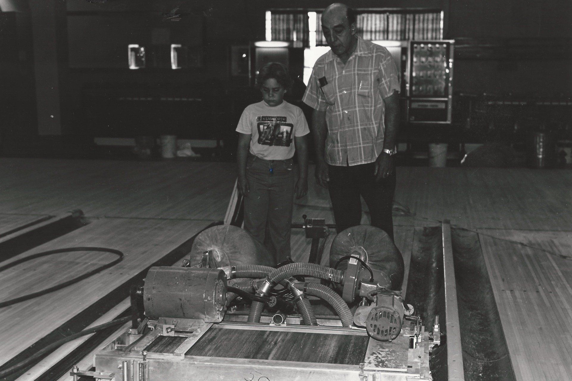 A man and a woman are standing next to a machine in a bowling alley.