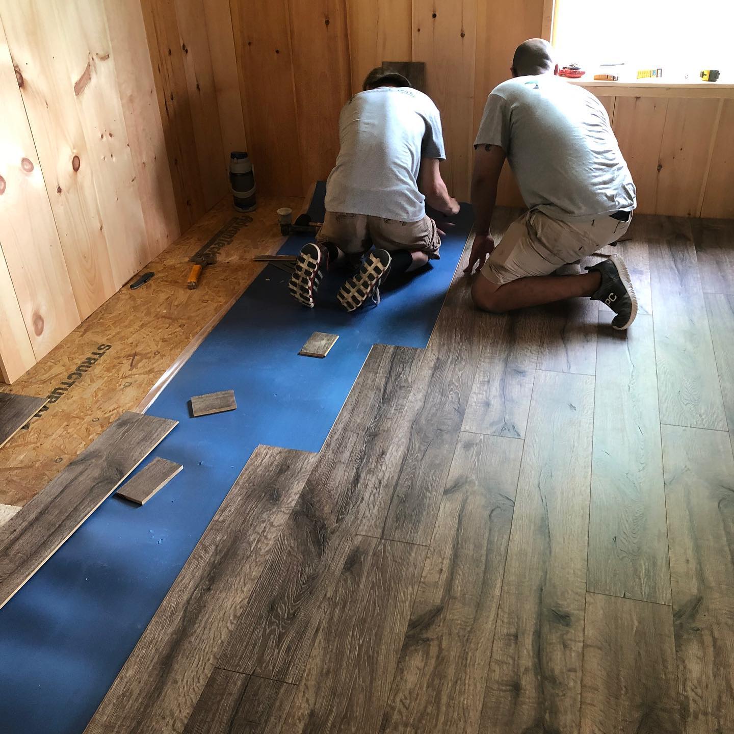 Two men are working on a wooden floor in a room.