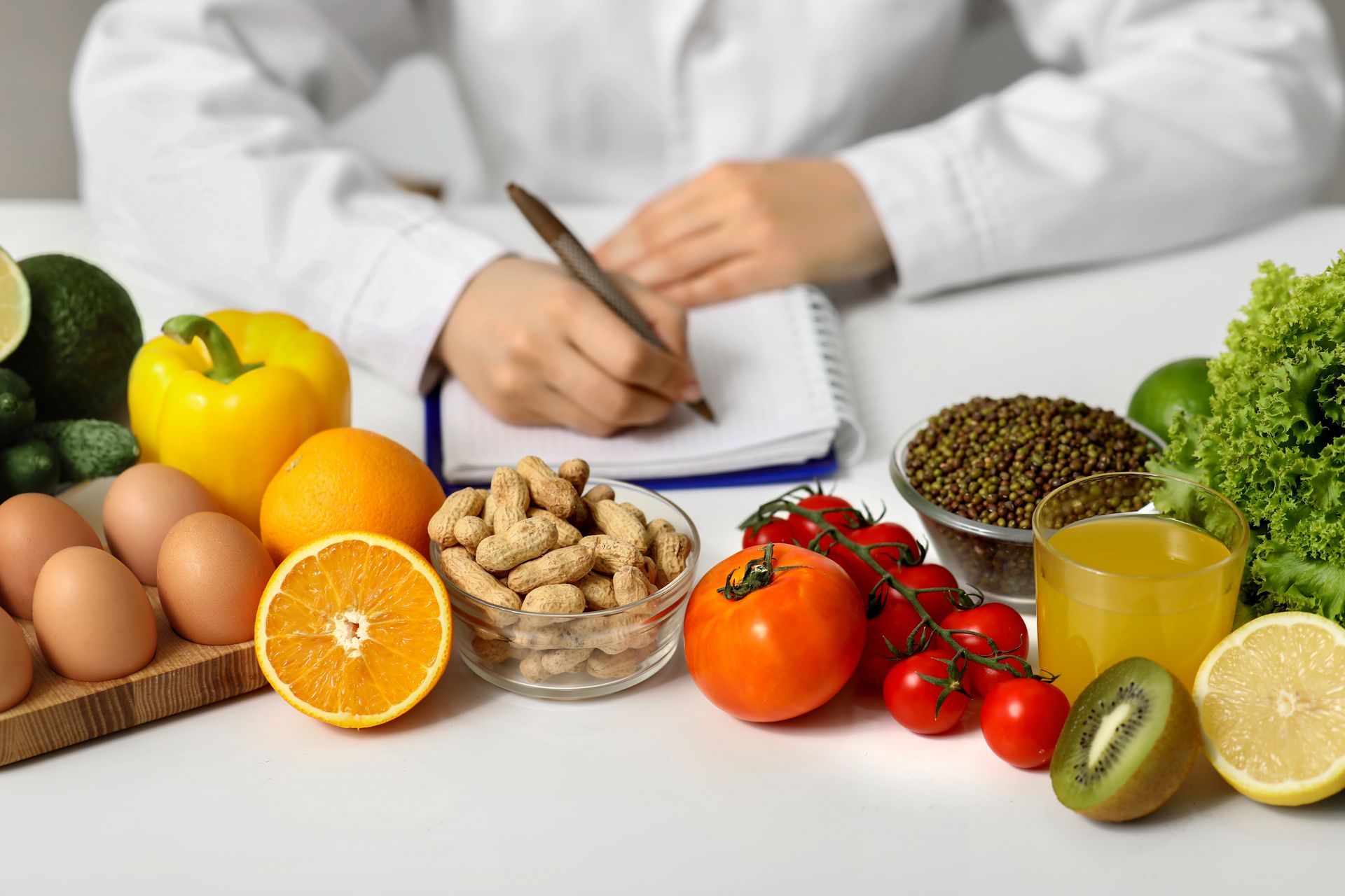 Dietitian at desk writing in notebook, surrounded by fresh fruits, vegetables, eggs, and nuts.