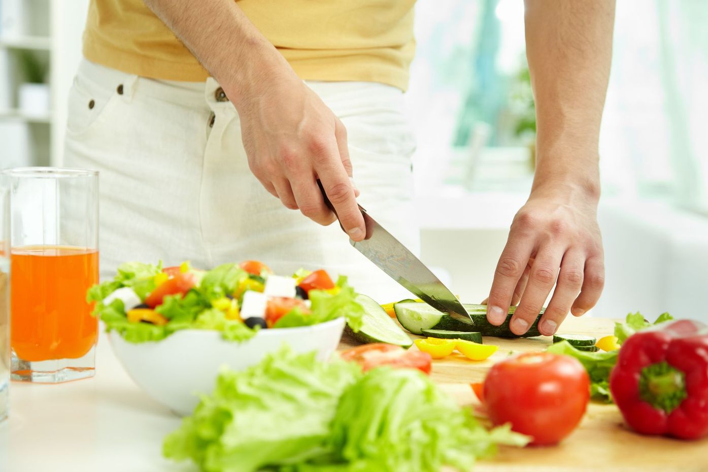 Person slicing cucumber on cutting board, preparing salad with vegetables.