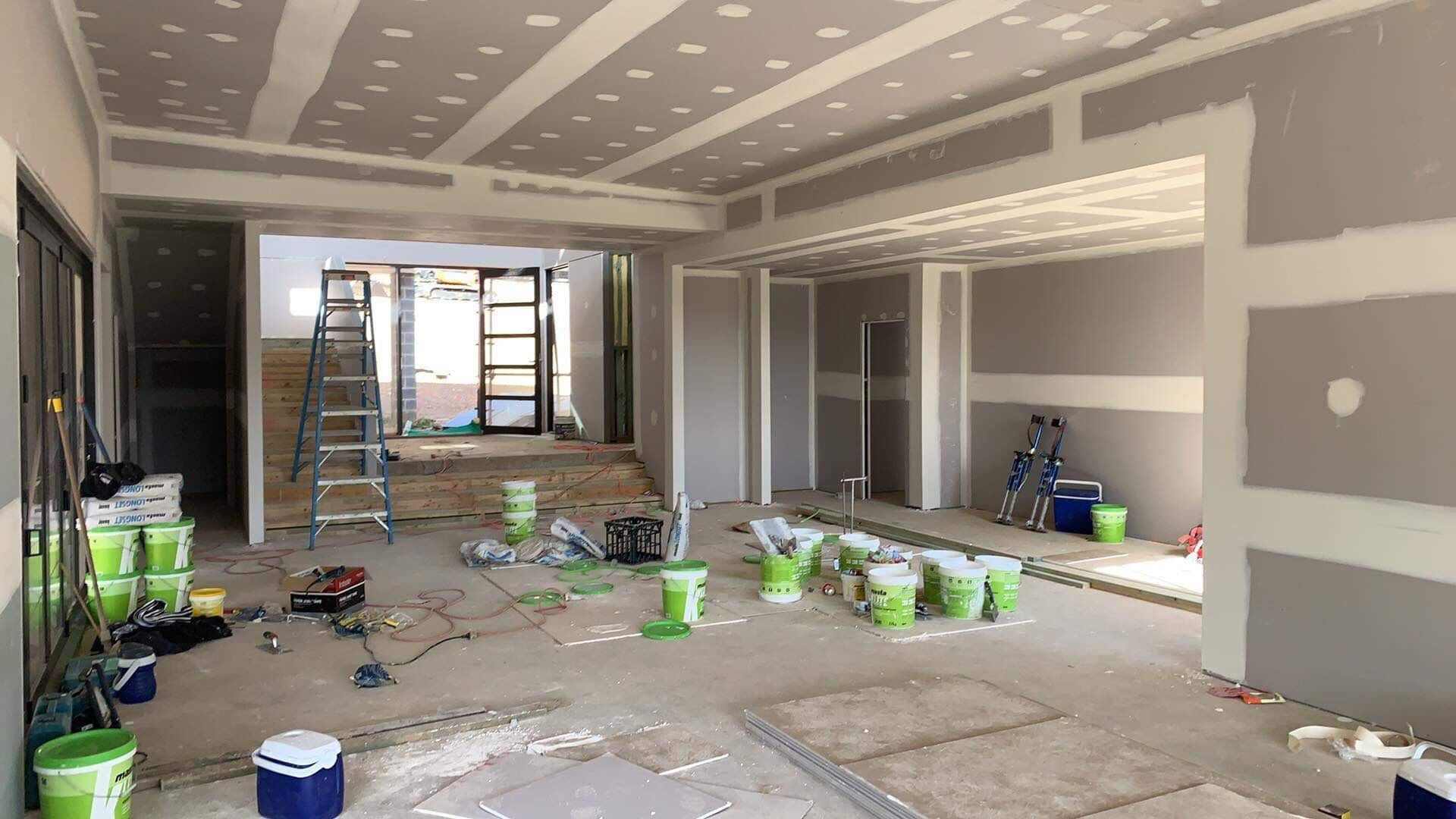 A Large Room Under Construction With Buckets of Paint on The Floor — Plaster Installation in Bensville, NSW