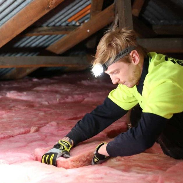 A Man Is Retrofitting Pink Batts Insulation In A Ceiling — Austral Insulation In Toormina, NSW