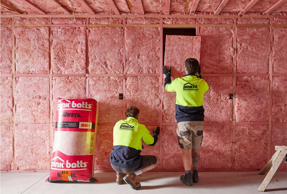 Two Men Installing Panels Of Pink Batts Insulation In A Wall — Austral Insulation In Toormina, NSW