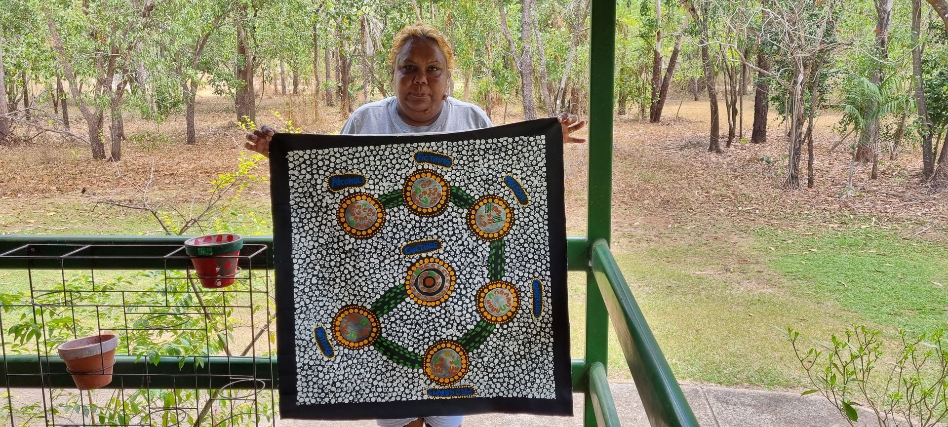 A woman is standing on a porch holding a painting.