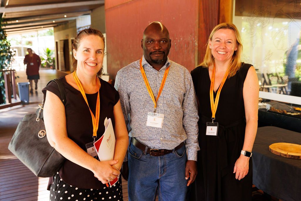 Three people wearing conference lanyards pose for a photo at an indoor venue.