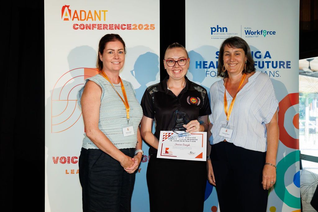 Three individuals stand smiling at the AADANT Conference 2023, with the center person holding an award certificate.