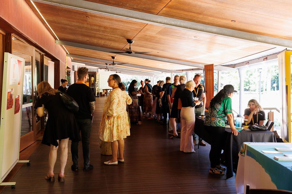 People gather in an open-air pavilion, some standing by tables and others looking at a display on a white board.