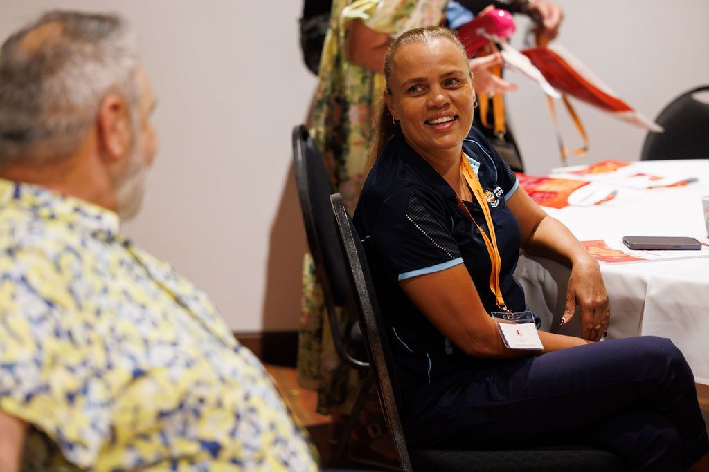 Two people sitting at a table in a room, with one individual smiling toward the other in conversation.