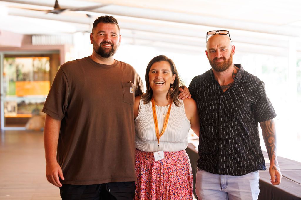 Two men and one woman stand smiling side-by-side in a well-lit indoor area.