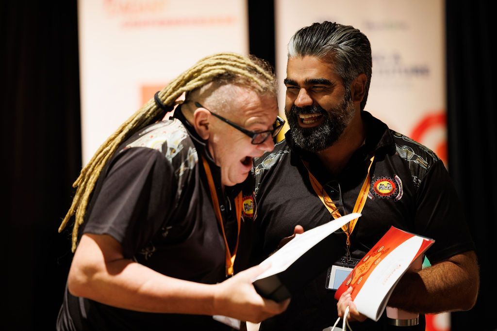 Two people wearing black shirts and conference lanyards look excitedly at a document together in a brightly lit room.