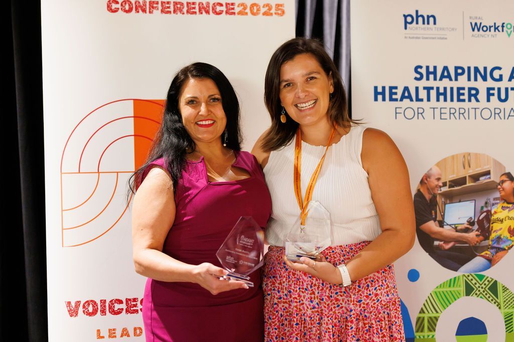 Two people smiling while holding awards in front of a conference banner for 