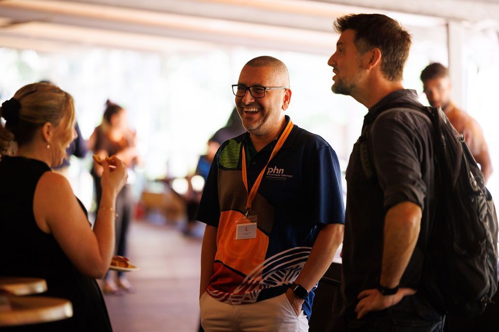 Three people stand in a bright, indoor space, smiling and engaged in conversation during a social event.