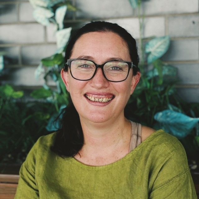 A woman wearing glasses and a green shirt is smiling